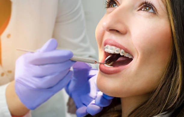 Closeup of beautiful girl with dental braces check up, satisfied smiling, while doctor looking her teeth
